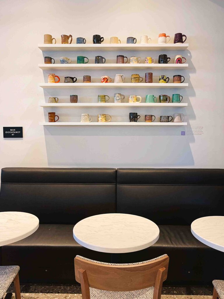 Minimalist coffee shop with shelves of coffee mugs available for purchase from local artists