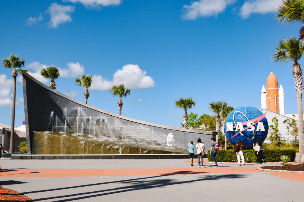 Entrance to Kennedy Space Center with large fountain wall, NASA globe, and rocket shuttle in the background